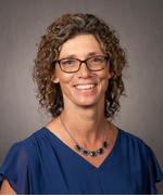 Photo of woman smiling wearing glasses and blue blouse.