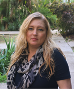 A woman with long blond hair, a dark shirt, and a scarf smiles at the camera.