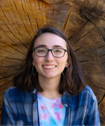 A girl with medium length brown hair and glasses smiles at the camera.