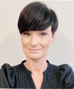 A woman with a dark brown hair bob smiles at the camera wearing a black shirt with puffy sleeves